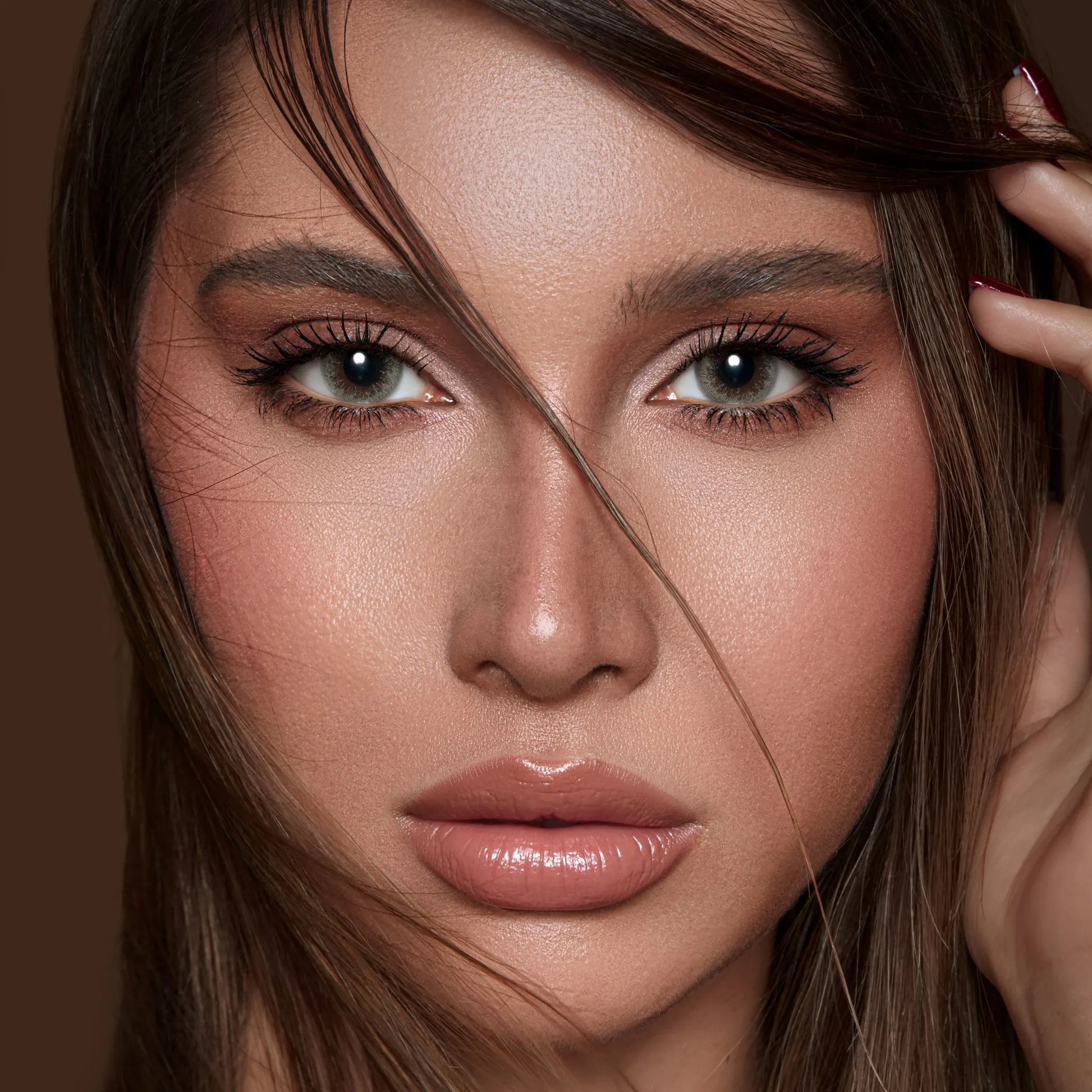 Close-up of a woman with brown hair and makeup against a brown background